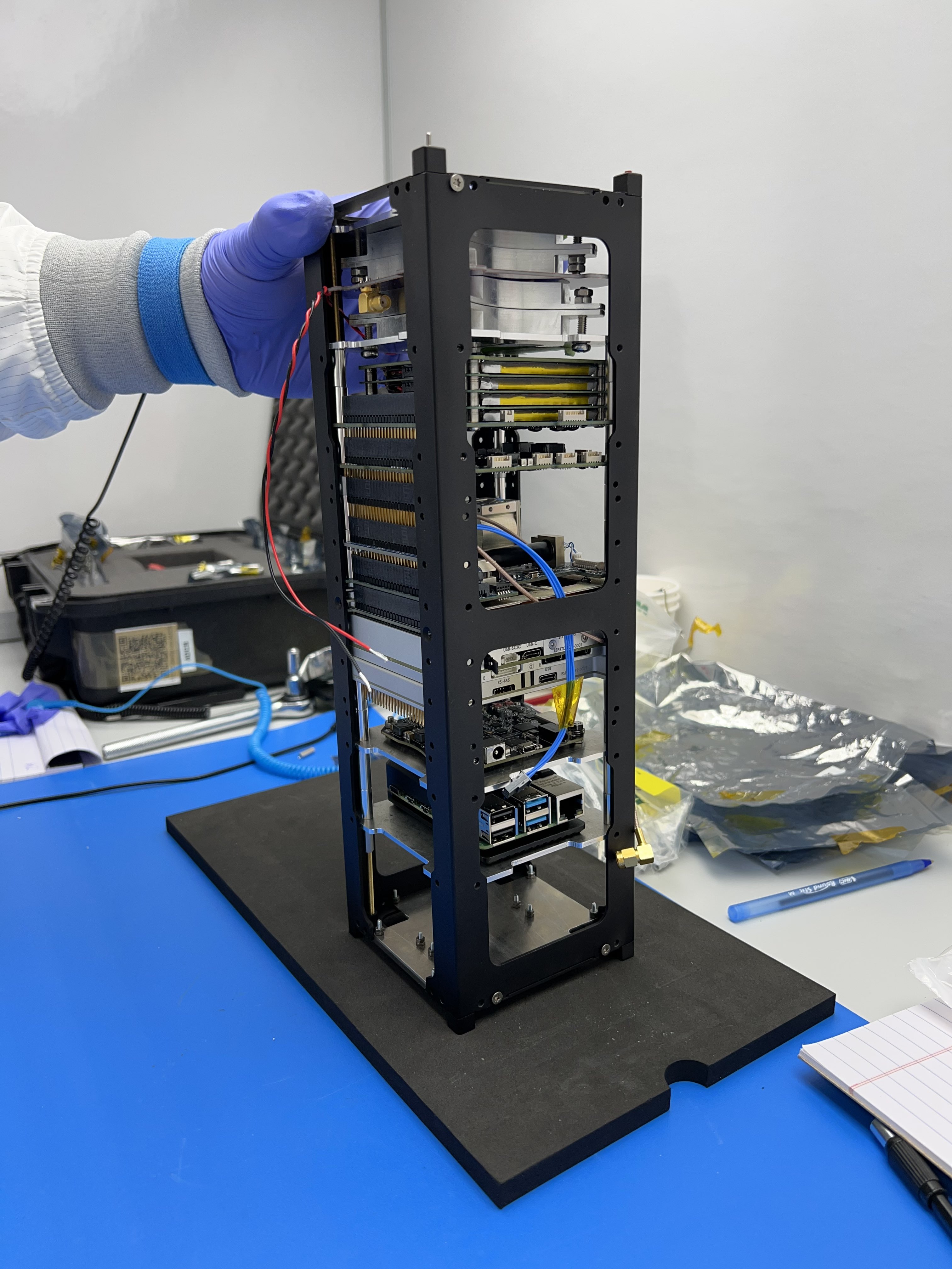 A partially assembled KUbeSat1 with internal structure and black metal frame. This image depicts the satellite being held up vertically on a black piece of foam which rests upon a blue platform.